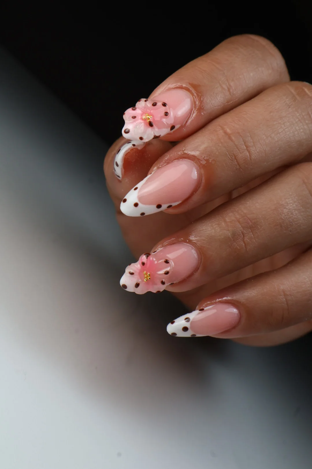 Manicura nude con detalles florales y puntos negros.