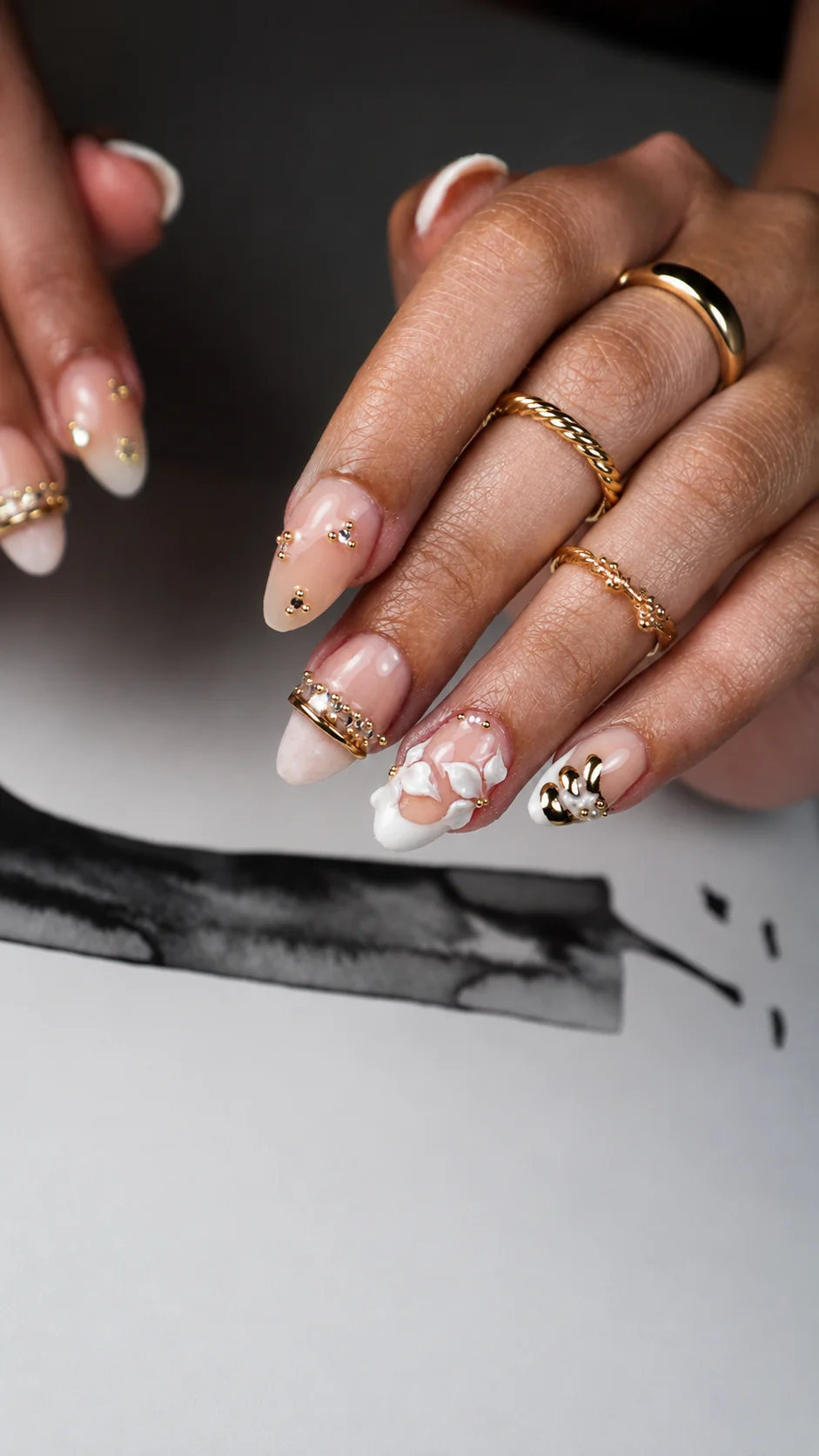 Uñas almendradas largas con relieve floral y detalles dorados sobre fondo oscuro.