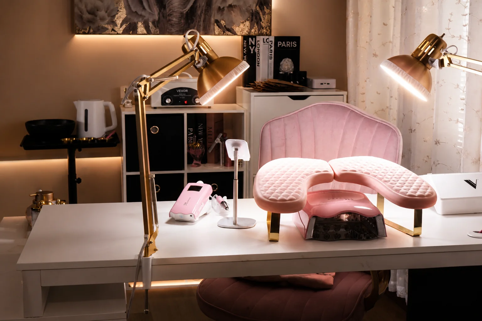 Mesa de trabajo del estudio con lámparas doradas, lámpara de curado y silla rosa.