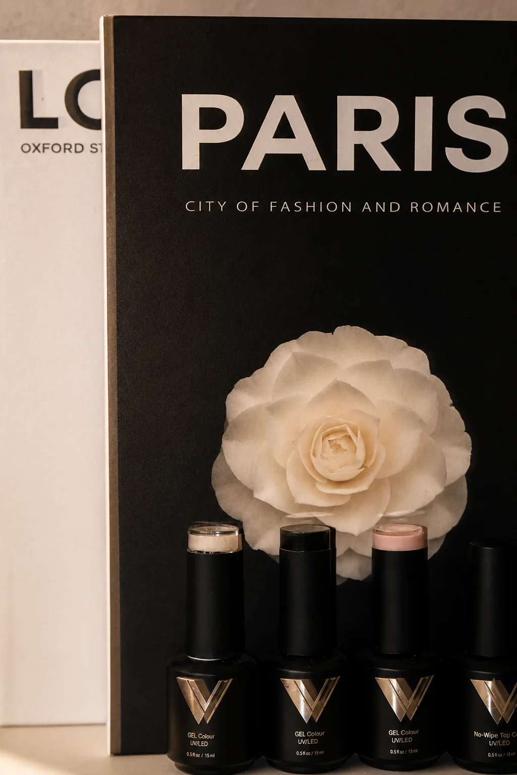 Esmaltes en gel negros y dorados junto a una rosa blanca y libros de mesa.
