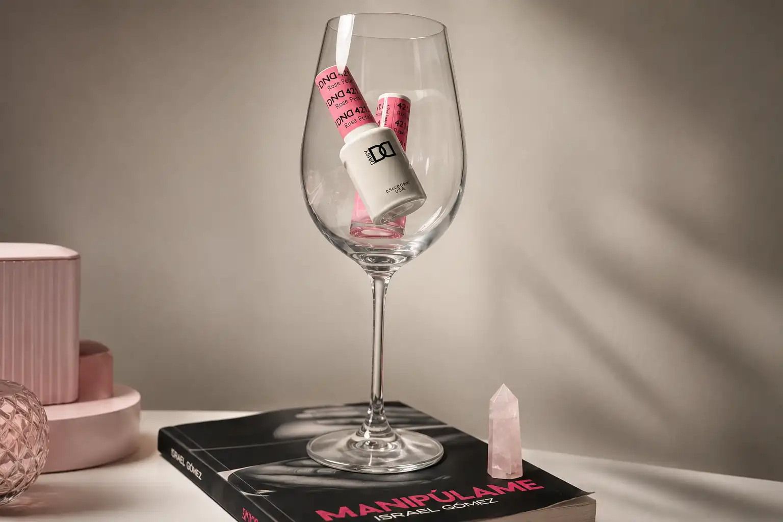 Copa de cristal con esmaltes en tonos rosa, apoyada sobre un libro en el estudio.